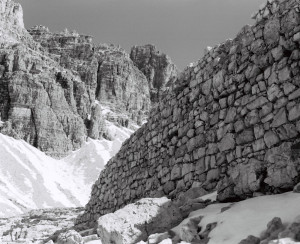 Blick auf eine Felswand gegenüber den Drei Zinnen (Dolomiten), im Vordergrund eine Mauer aus Bruchsteinen